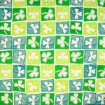 A patterned fabric features a grid of squares in varying shades of green and blue each containing a white clover design creating a vibrant and playful textile.