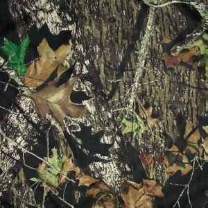 A patterned surface resembling tree bark and leaves blends into a dark background showcasing a mix of brown and green foliage with scattered twigs creating a camouflage effect.