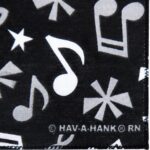A black fabric features various white musical notes and stars printed across its surface creating a lively pattern along with a logo at the bottom right corner that reads © HAV-A-HANK® RN