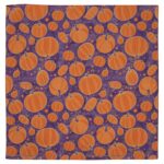 A fabric with a repeated pattern of varying sizes of orange pumpkins set against a purple background featuring swirls and small dots  creating a seasonal decorative theme.