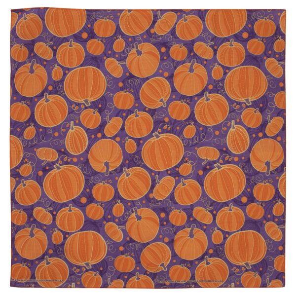 A patterned fabric features various sizes of orange pumpkins scattered across a purple background with spiral designs and small circles  creating a festive autumnal theme.