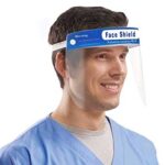 A man wearing a blue medical scrub smiles while donning a clear face shield that has a warning label on its headband indicating protective use in environments requiring isolation.